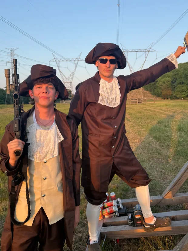Two team members in colonial costumes posing in a field at golden hour