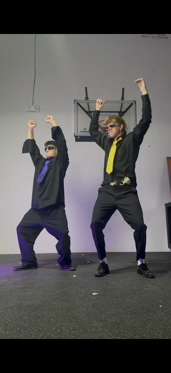 Two team members in suits and sunglasses striking a dance pose mid-shoot