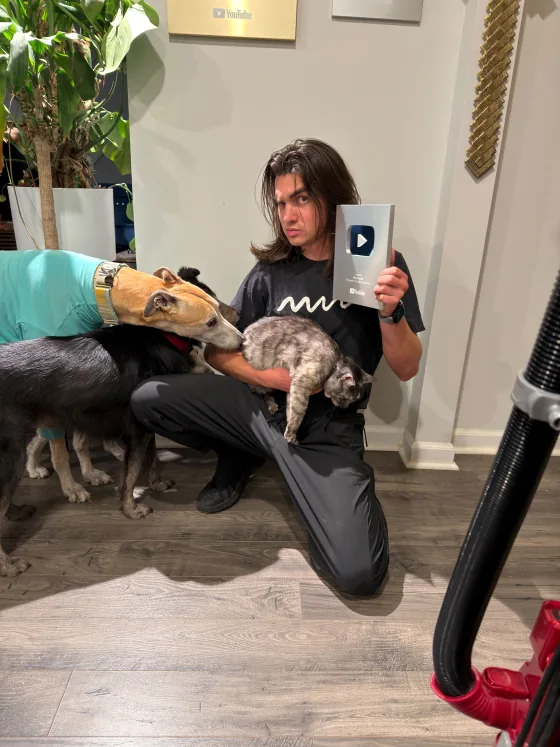 Team member holding a silver YouTube play button while two dogs and a cat pile on