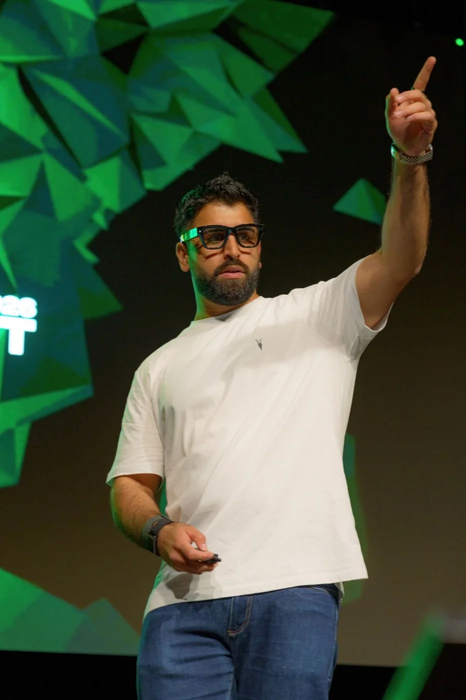A speaker on stage at the AI Summit in front of a green geometric backdrop