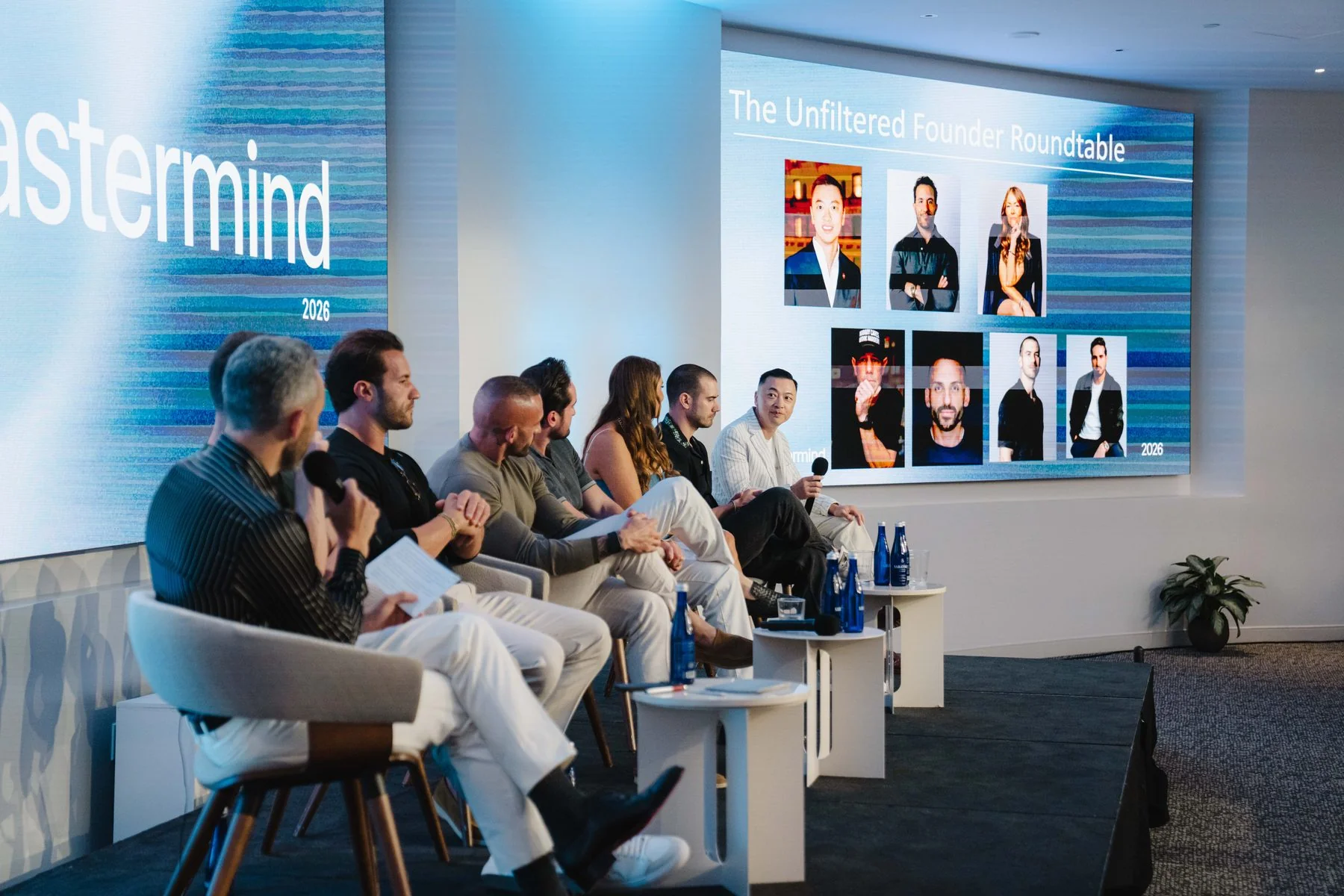 Panel of founders on stage at the NYC Mastermind, in front of an Unfiltered Founder Roundtable screen